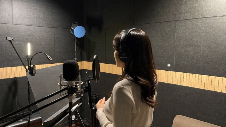 헤드폰을 끼고 녹음 부스에 서 있는 여성